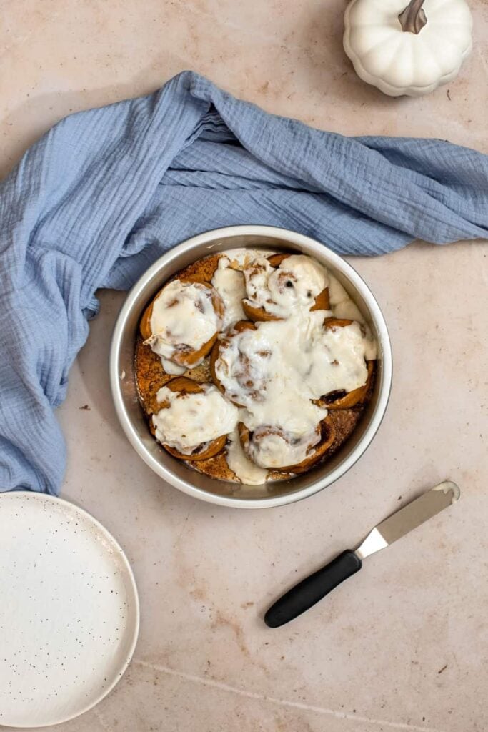 pumpkin cinnamon rolls with maple cream cheese icing in a round silver pan