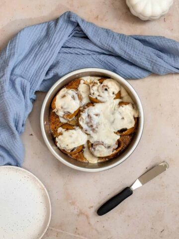 pumpkin cinnamon rolls with maple cream cheese icing in a round silver pan