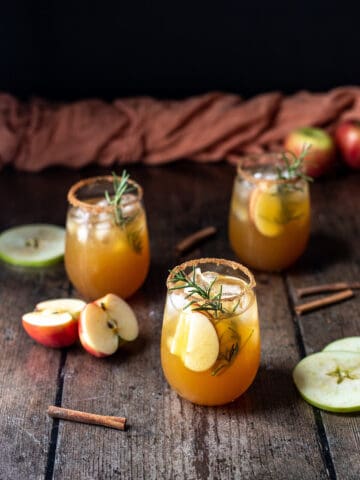three apple cider margaritas in stemless wine glasses on a wooden background.