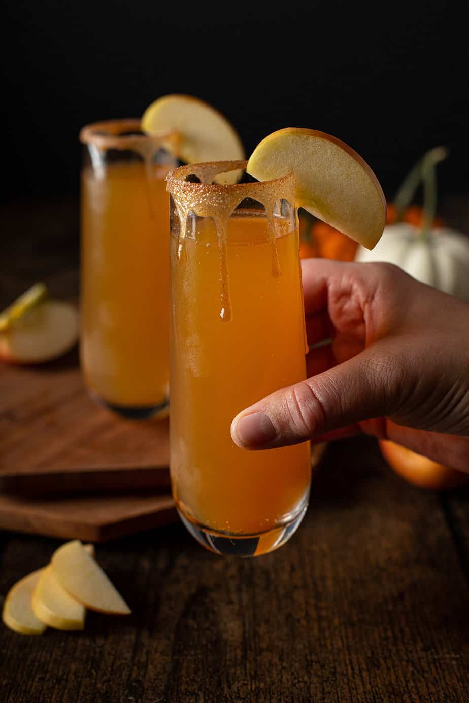 a hand holding a stemless champagne flute of apple cider mimosas