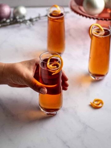 three chambord kir royale cocktails with orange twists; a hand is reaching for one