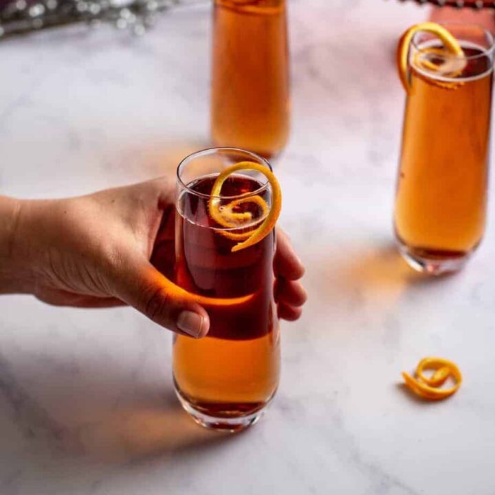 three chambord kir royale cocktails with orange twists; a hand is reaching for one