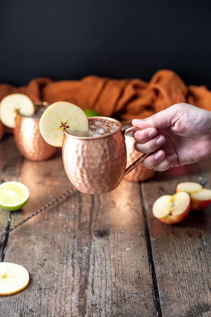 a hand holding a caramel apple moscow mule