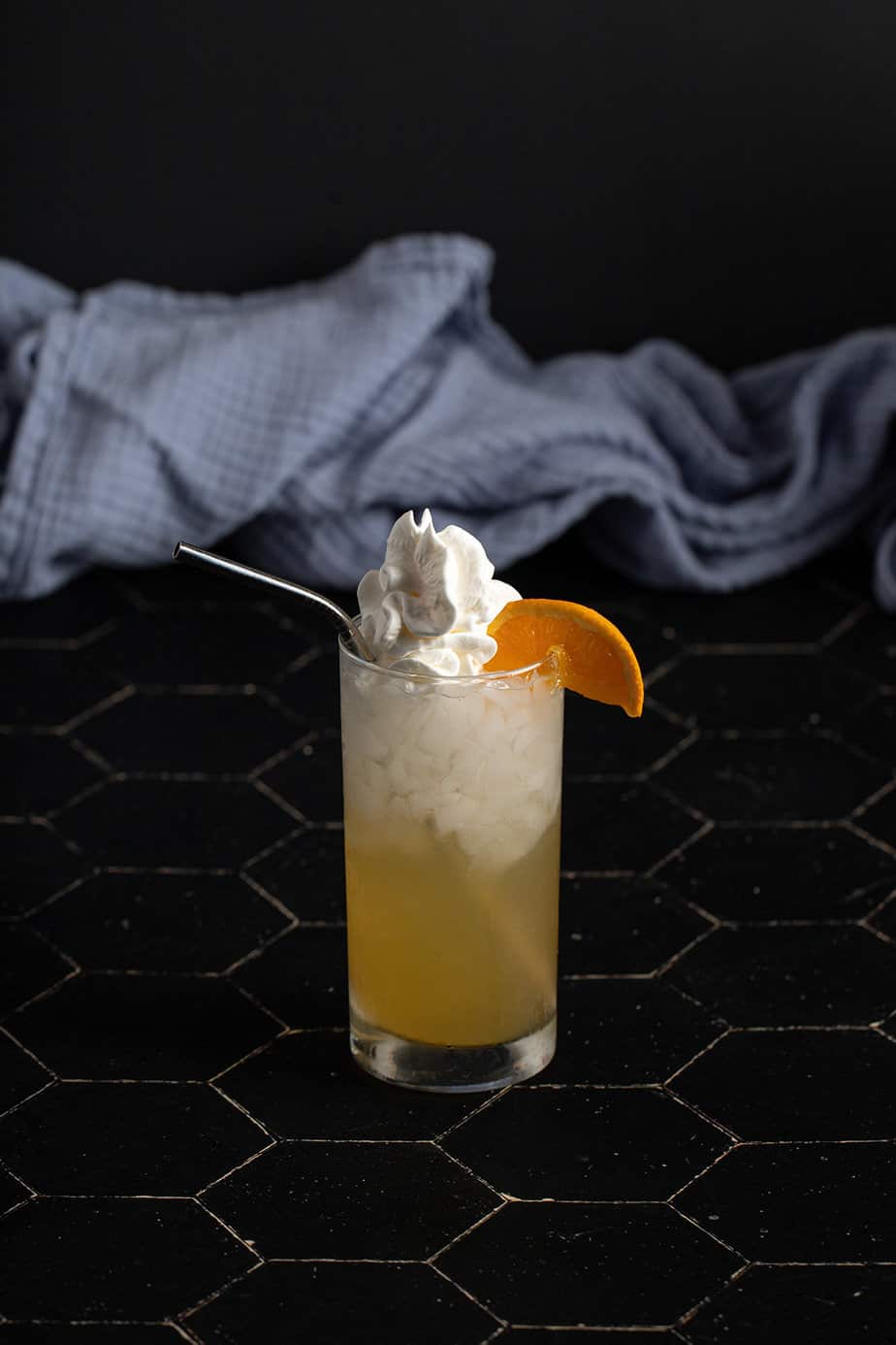 an orange creamsicle crush garnished with whipped cream and an orange wedge, plus a metal straw