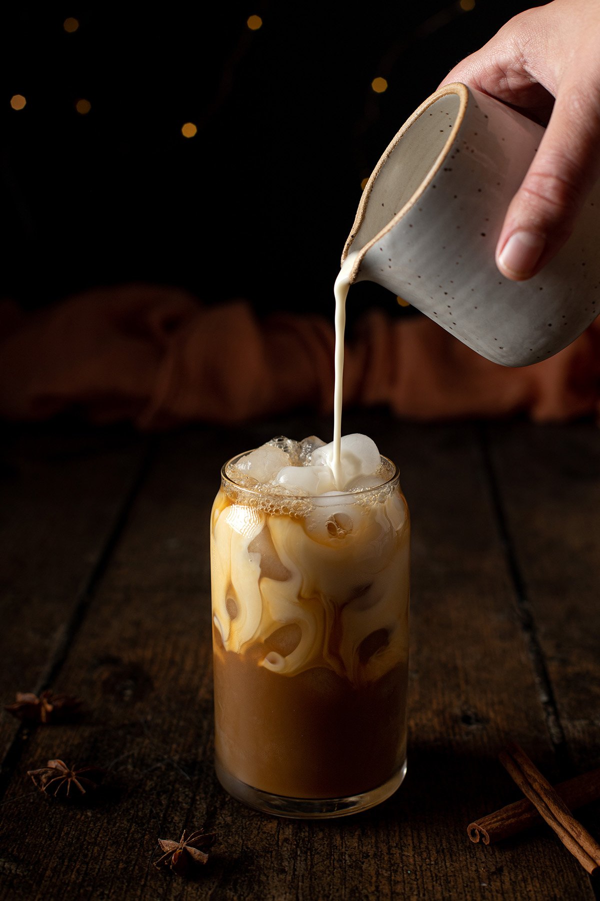 oat milk being poured into an iced chai latte