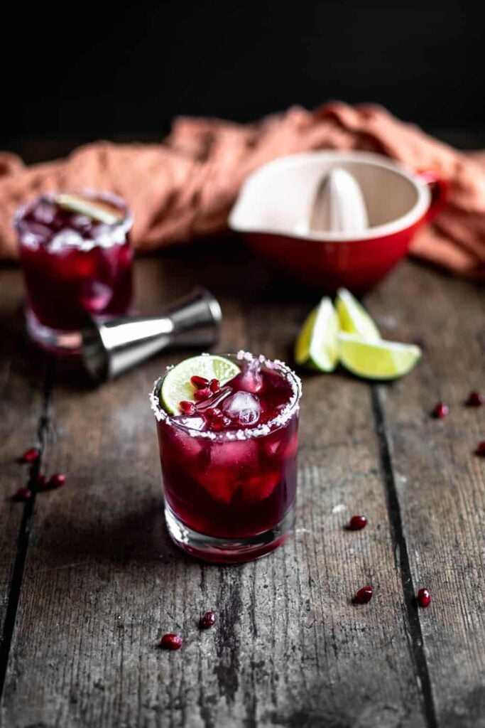 two pomegranate margaritas in short glasses on a dark wooden table