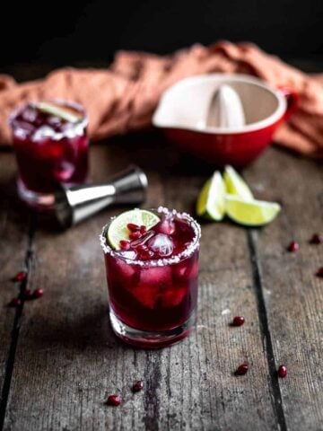 two pomegranate margaritas in short glasses on a dark wooden table