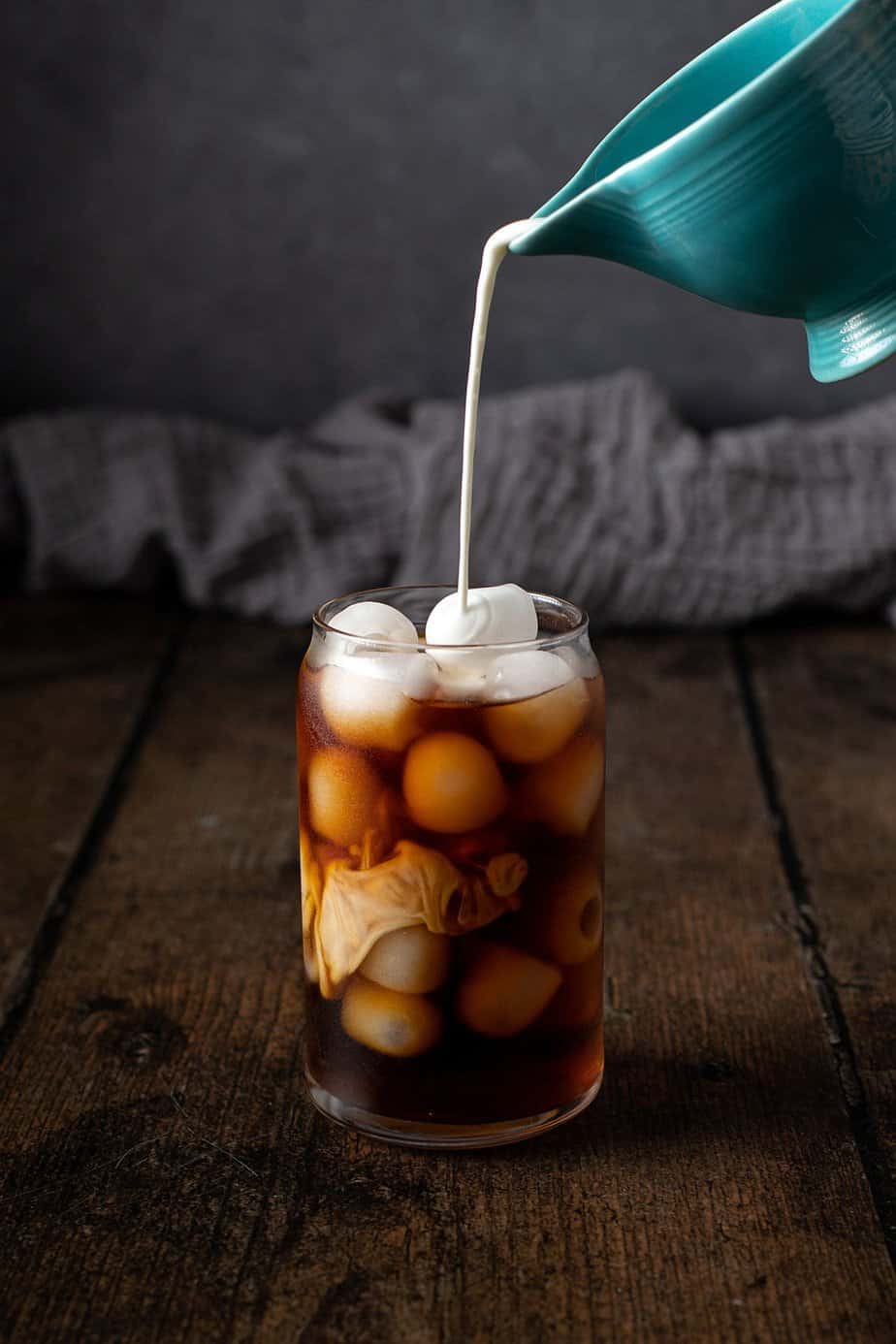 cream being poured into a glass of cold brew coffee