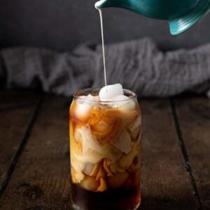 cream being poured into a glass of cold brew coffee