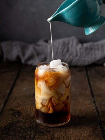 cream being poured into a glass of cold brew coffee