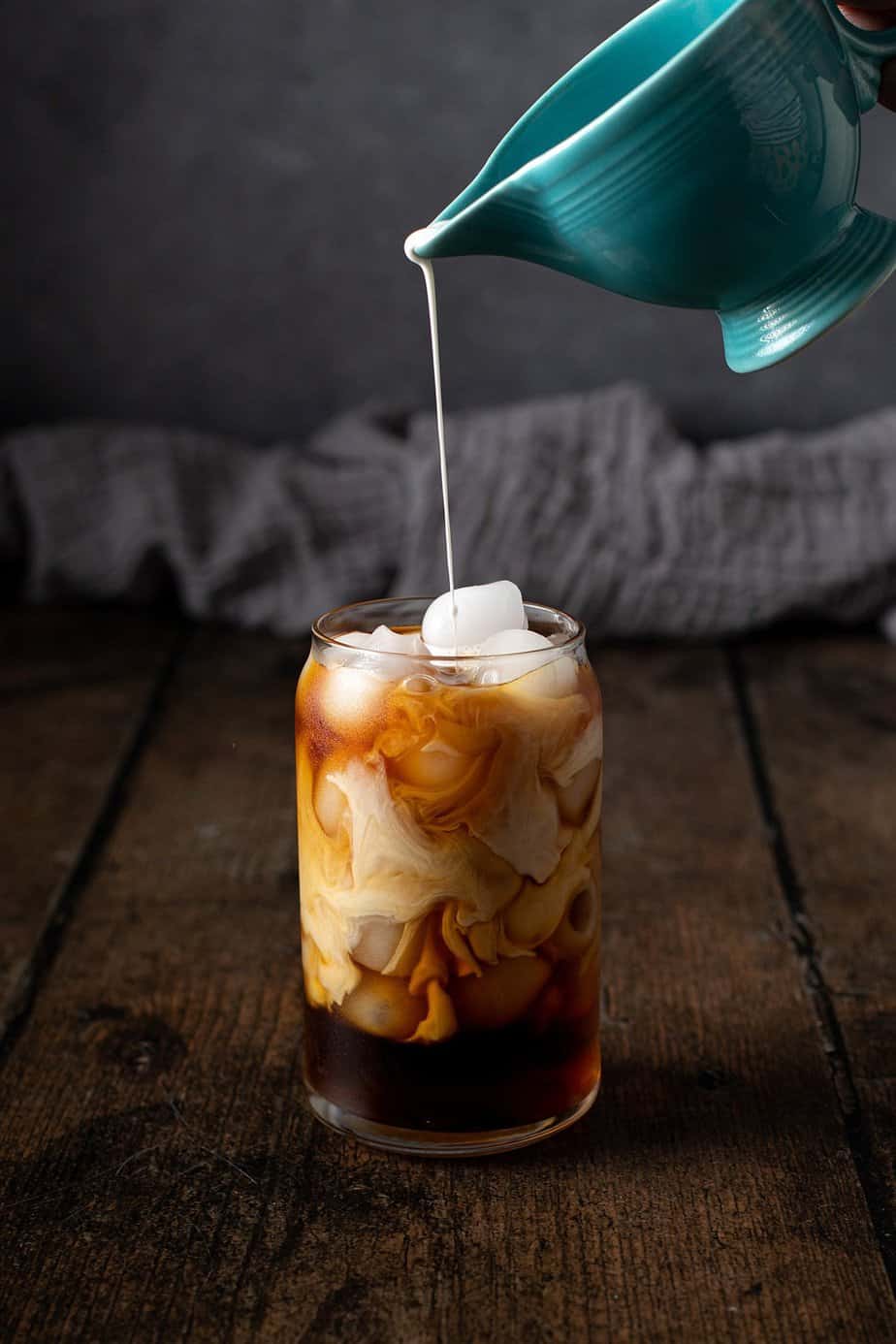 cream being poured into a glass of cold brew coffee