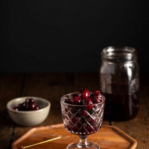 a small goblet full of luxardo cherries on a wooden tray