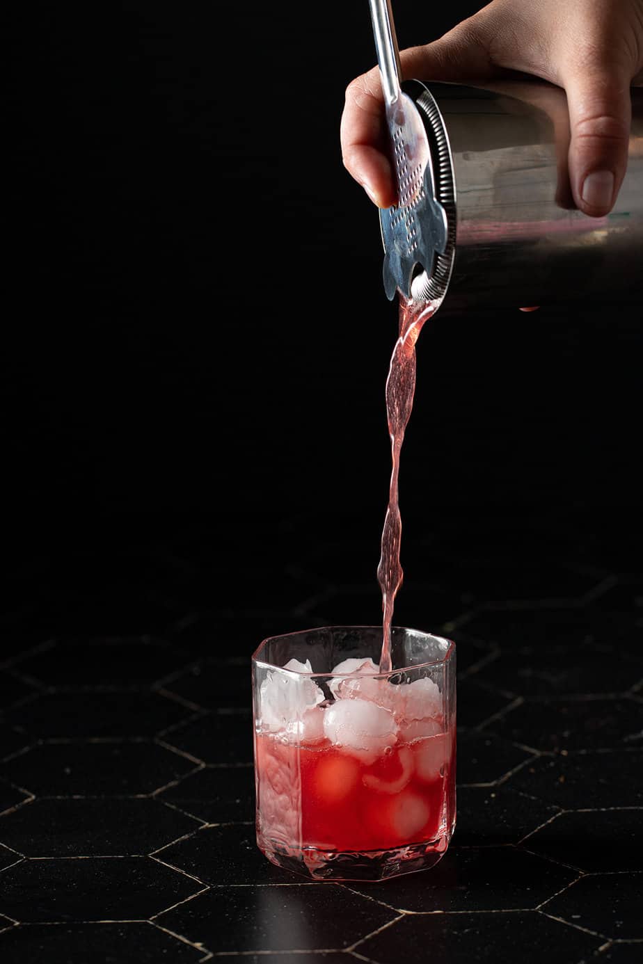 belmont jewel cocktail being strained into a rocks glass with ice