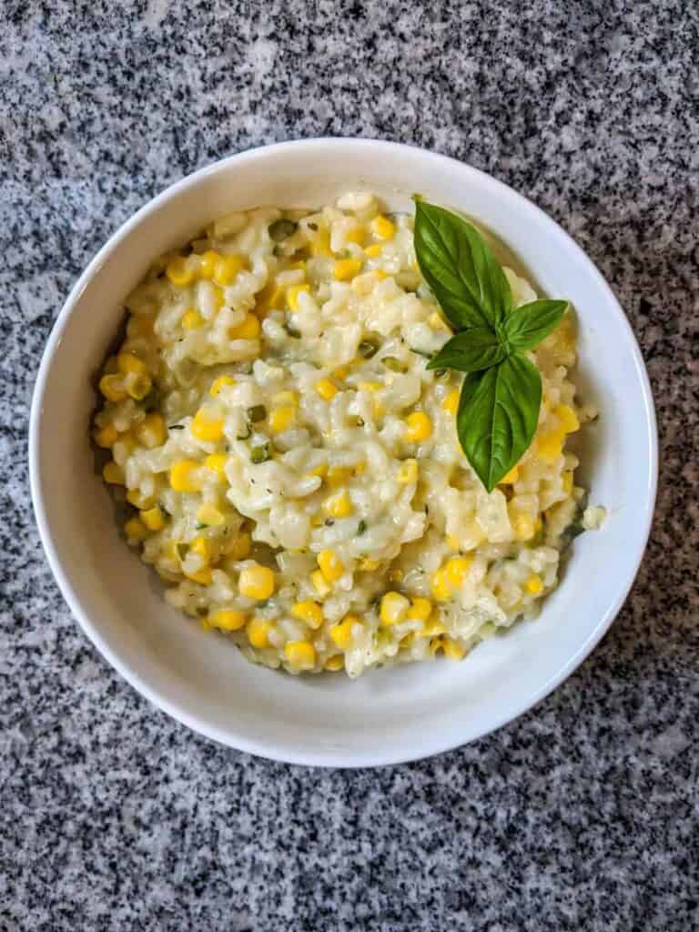 corn and jalapeño risotto in a white bowl on a black and white granite countertop