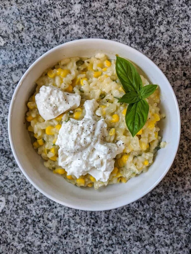 corn and jalapeño risotto, garnished with burrata cheese and fresh basil, in a white bowl on a black and white granite countertop