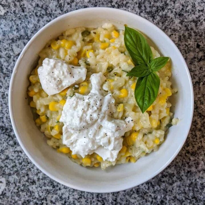 corn and jalapeño risotto, garnished with burrata cheese and fresh basil, in a white bowl on a black and white granite countertop
