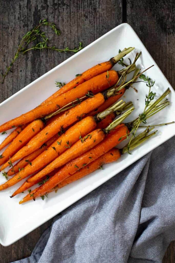 roasted petite carrots with green tops on a white serving dish