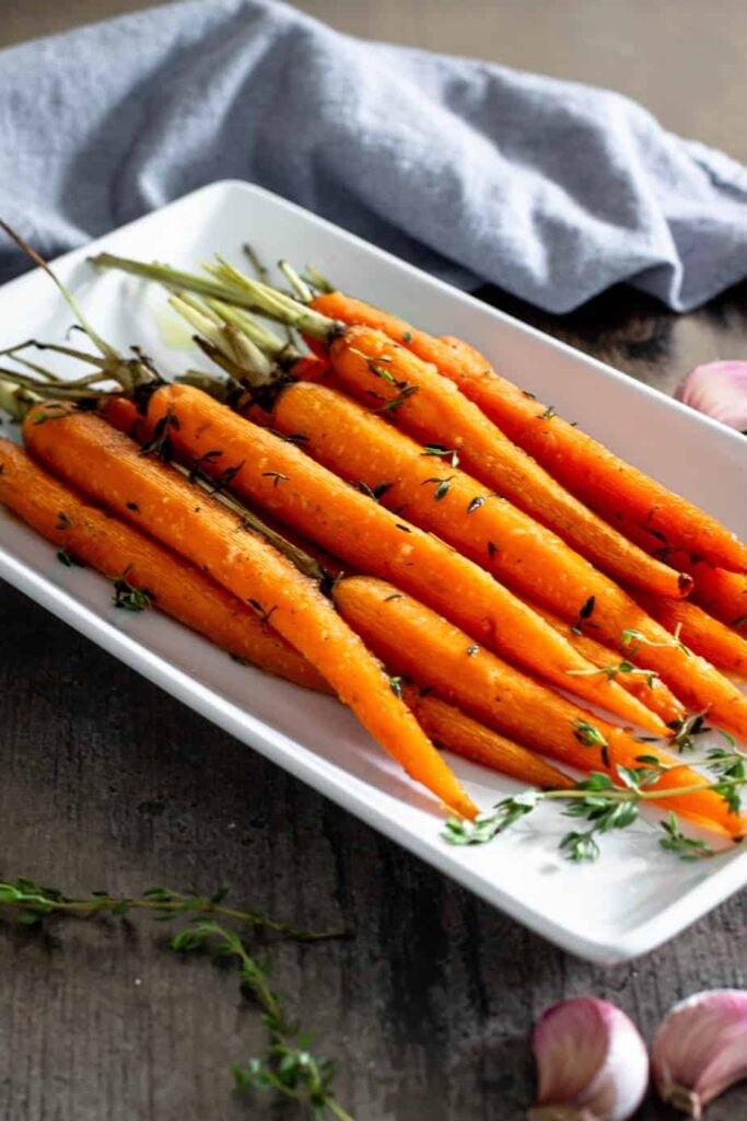 roasted petite carrots with green tops on a white serving dish