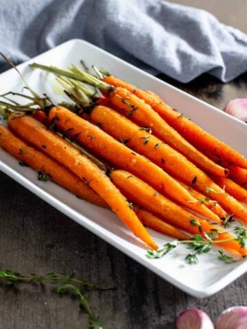roasted petite carrots with green tops on a white serving dish