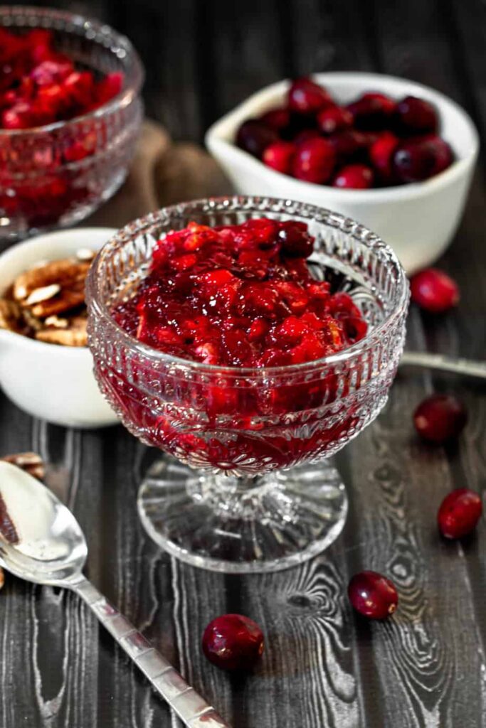 cranberry jello salad in a clear glass cup on a dark wood backdrop