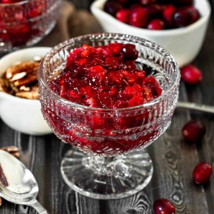 cranberry jello salad in a clear glass cup on a dark wood backdrop