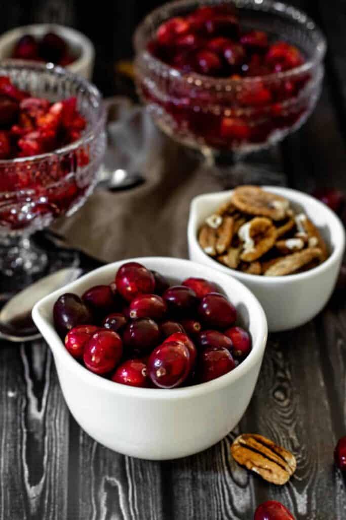 fresh cranberries in a white measuring cup on a wooden backdrop