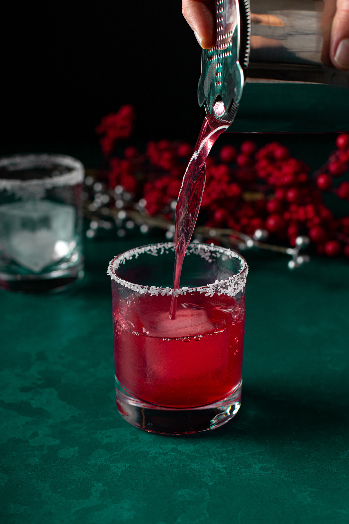 cranberry margarita being poured into a rocks glass with a salt rim