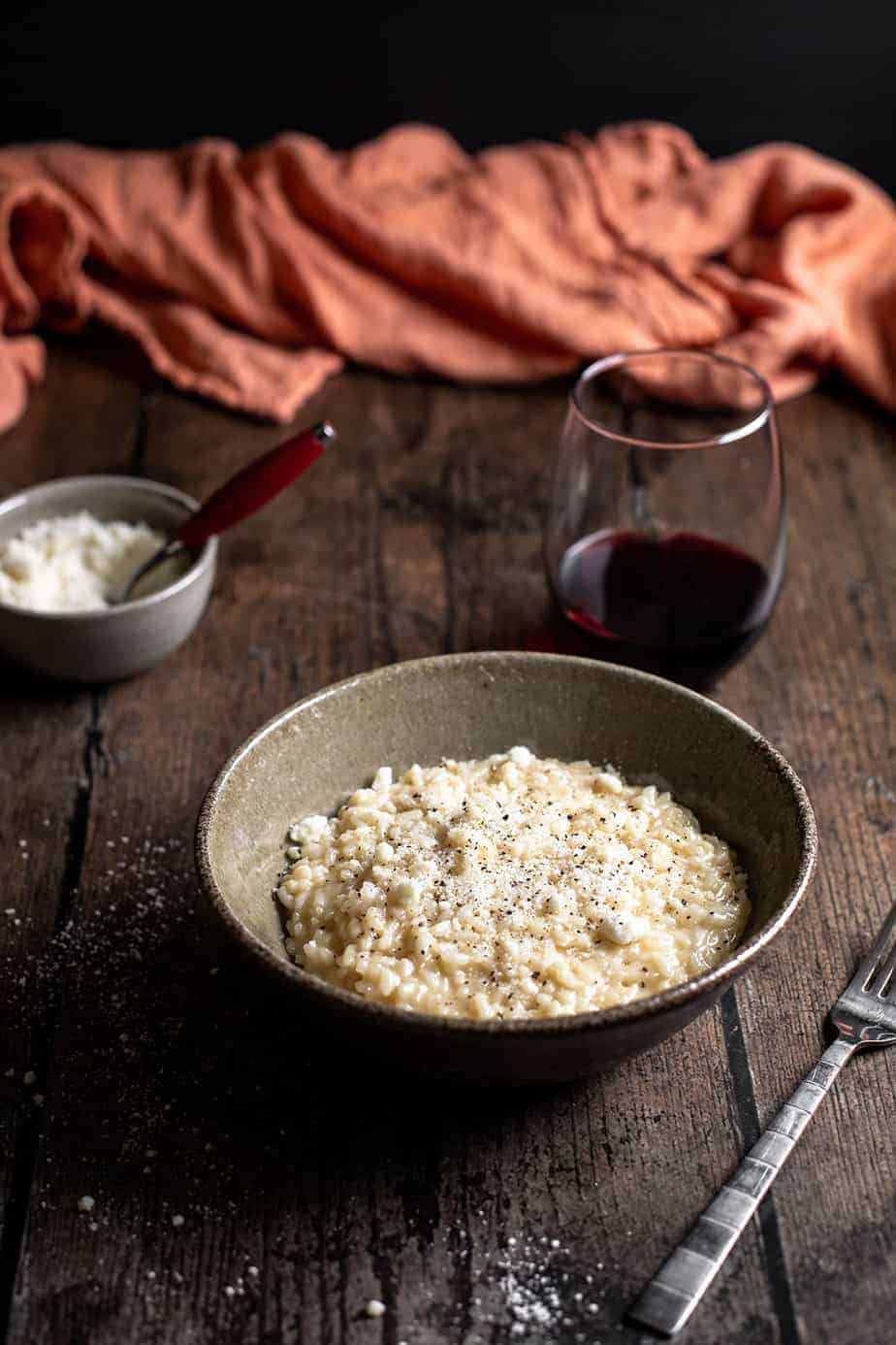 bowl of cacio e pepe risotto with glass of wine, dish of cheese in background