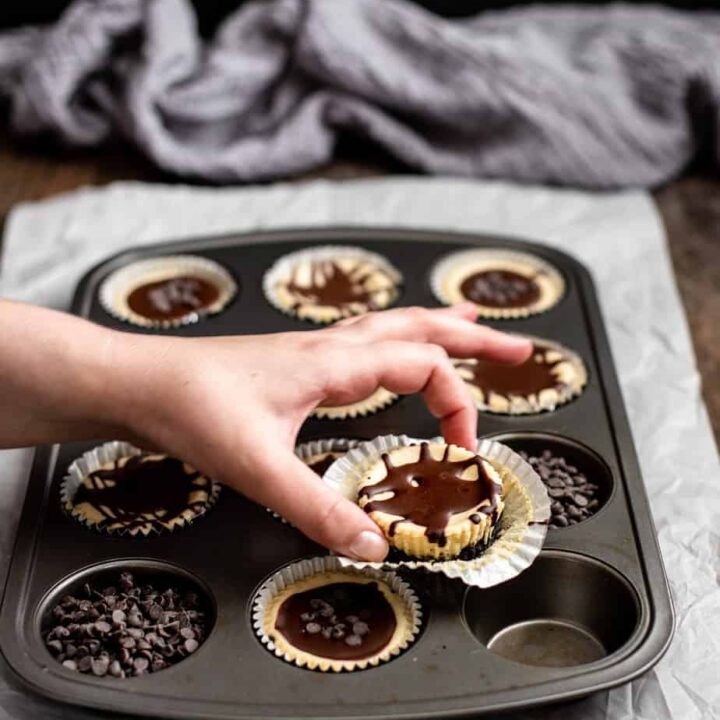 a muffin tin with mini cheesecakes, a hand is reaching for one