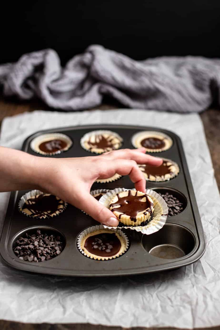 a muffin tin with mini cheesecakes, a hand is reaching for one