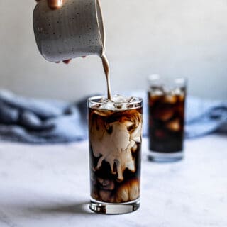 two glasses of iced coffee, a small pitcher is pouring cream into one