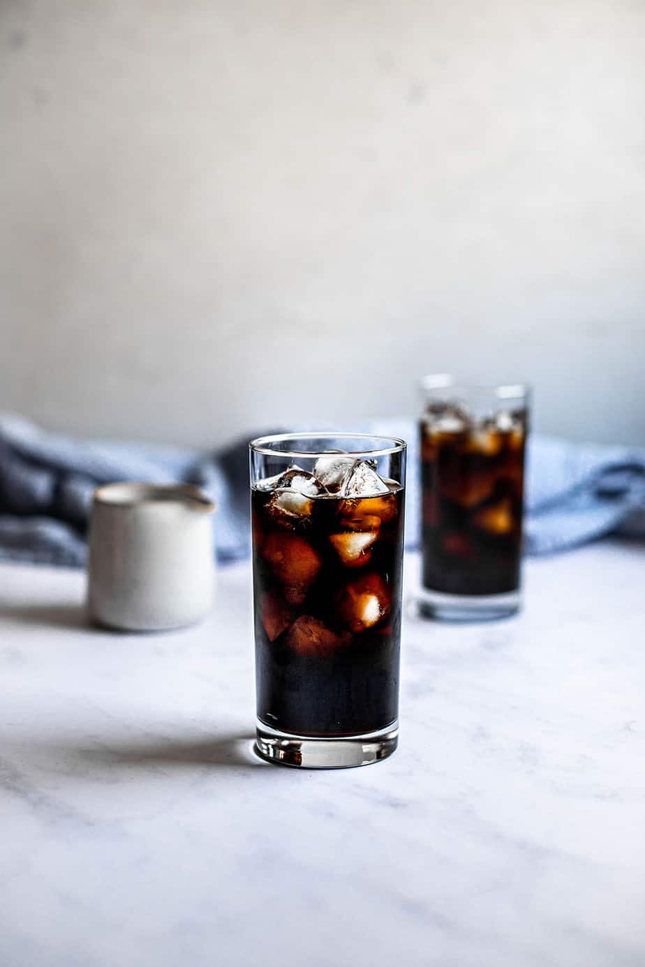 two glasses of iced coffee, a small pitcher is in the background