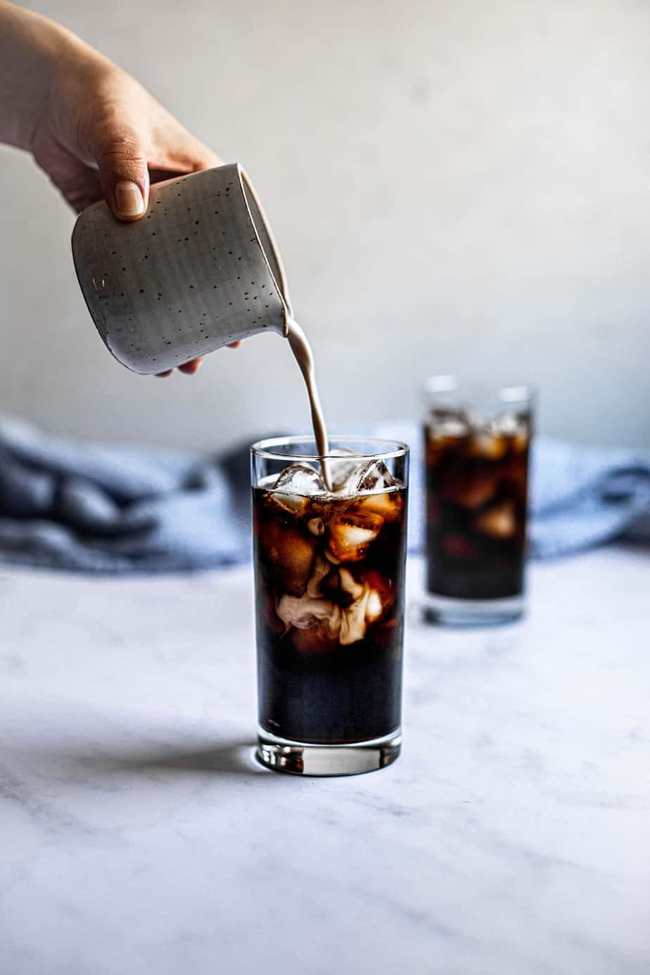 two glasses of iced coffee, a small pitcher is pouring cream into one