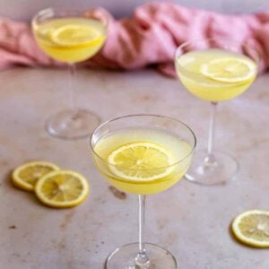 a 45 degree angle view of three limoncello martinis in coupe glasses, lemon slices on the table, lemon slices floating in the glasses