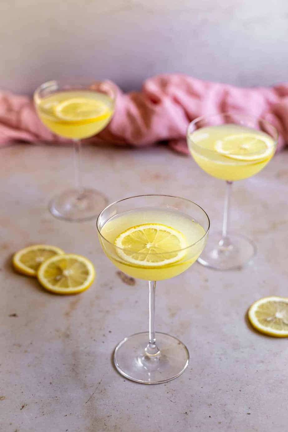 a 45 degree angle view of three limoncello martinis in coupe glasses, lemon slices on the table, lemon slices floating in the glasses