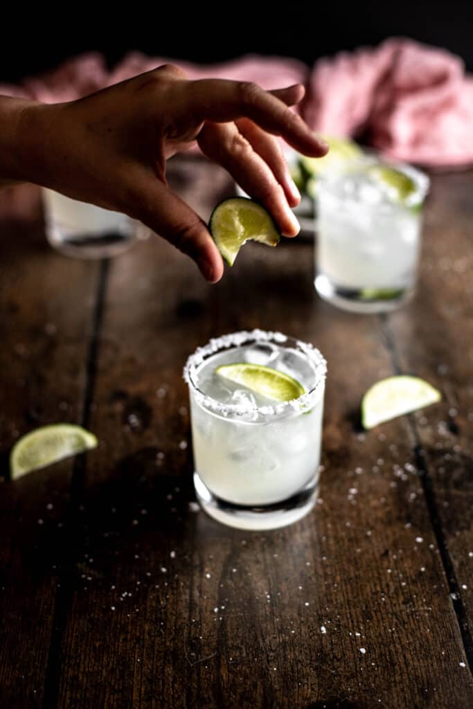 hand squeezing a lime wedge into a margarita