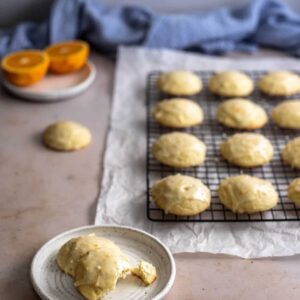 45 degree angle view of orange cookies on wire cooling rack, cookies on a small plate in lower left with bite taken out