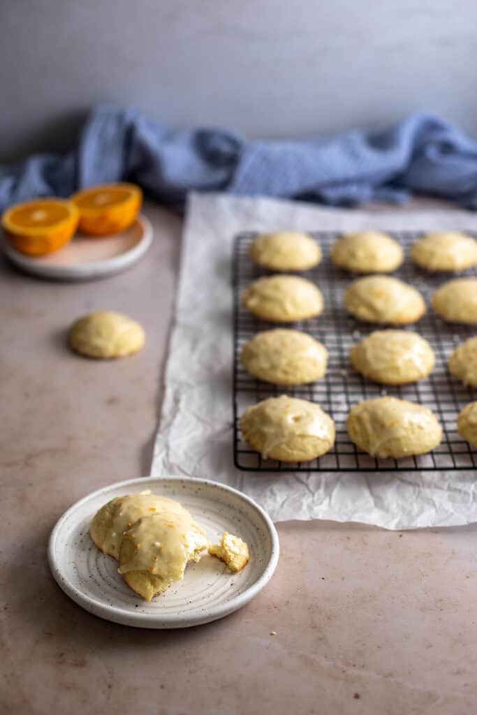 45 degree angle view of orange cookies on wire cooling rack, cookies on a small plate in lower left with bite taken out