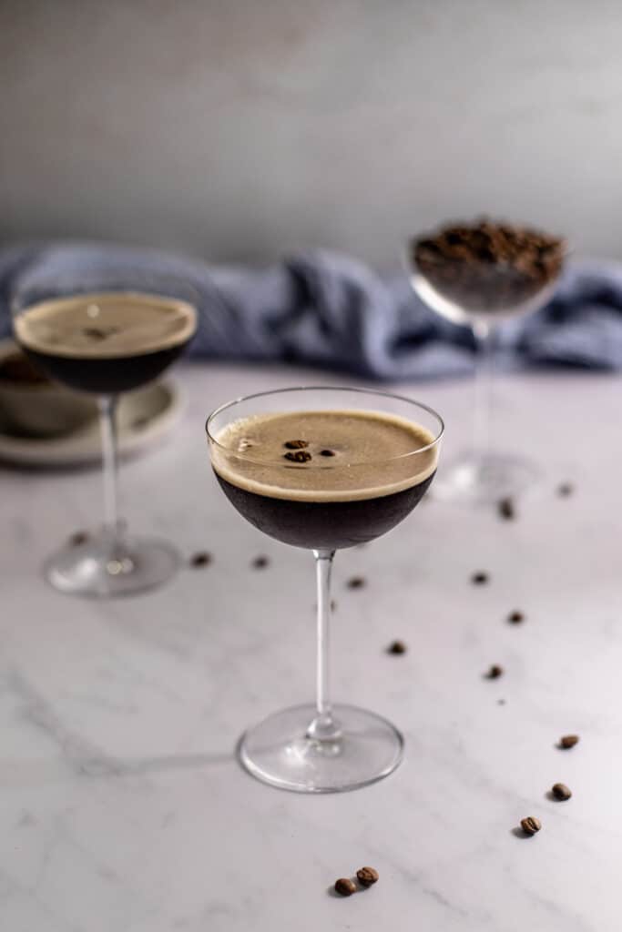 two espresso martinis in coupe glasses, one coupe glass filled with coffee beans