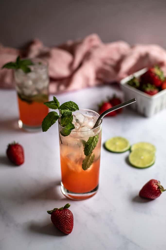 two strawberry mojitos, one with a metal straw, a small basket of strawberries in the background