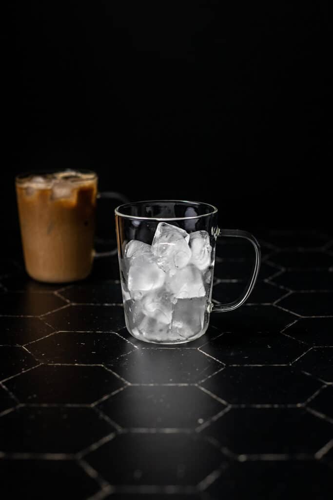 a clear glass mug filled with ice on a black background