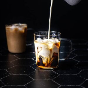 a clear glass mug filled with ice, espresso, and having milk poured into it