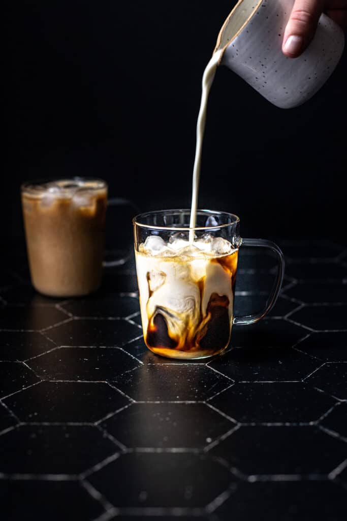 a clear glass mug filled with ice, espresso, and having milk poured into it