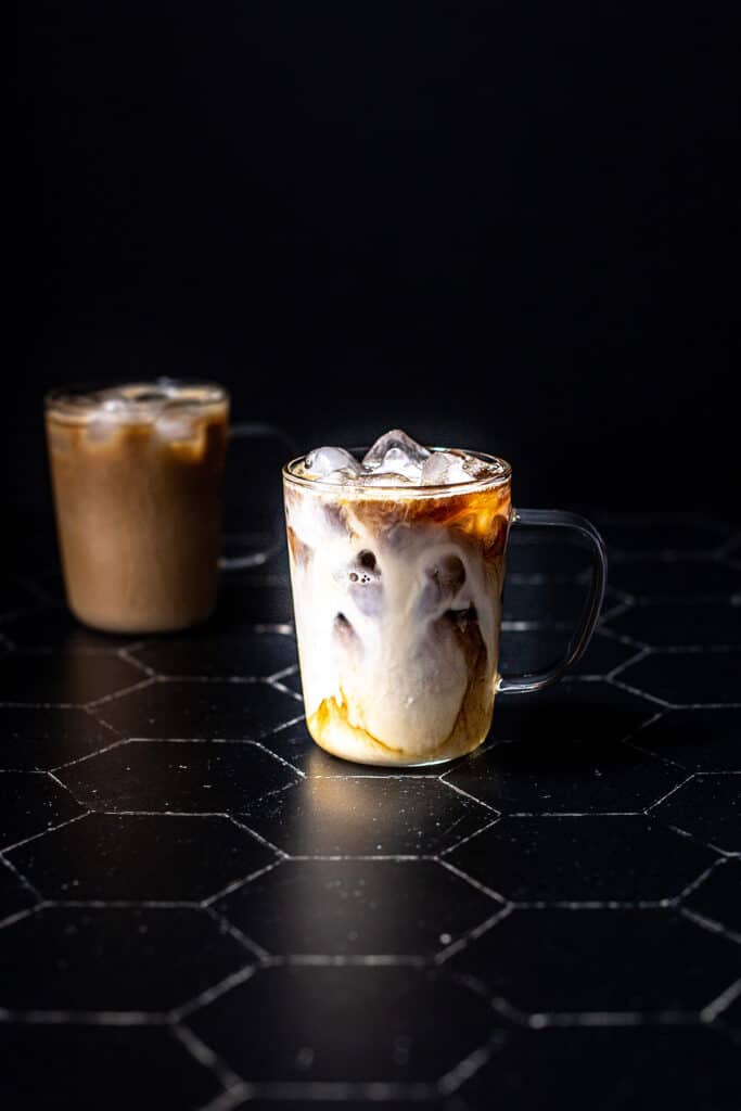 a clear glass mug filled with espresso and ice, milky swirls