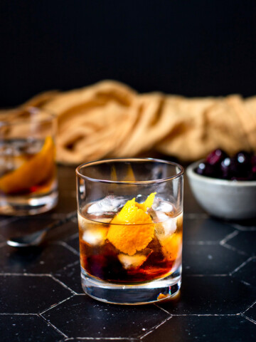 a maple old fashioned on a black tile background