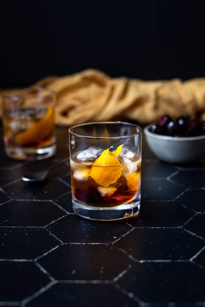 a maple old fashioned on a black tile background