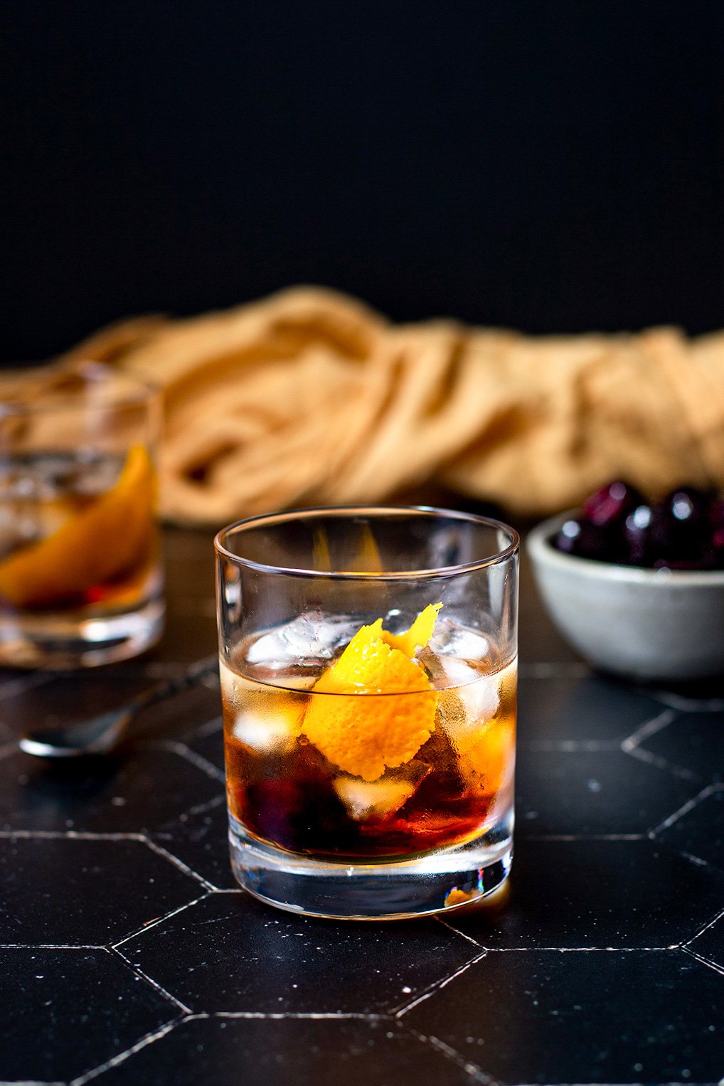 a maple old fashioned on a black tile background