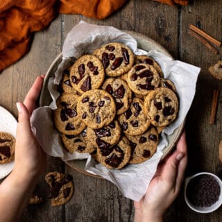 an overhead view of two hands holding a bowl of pumpkin spice chocolate chip cookies