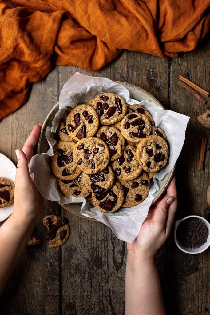 an overhead view of two hands holding a bowl of pumpkin spice chocolate chip cookies