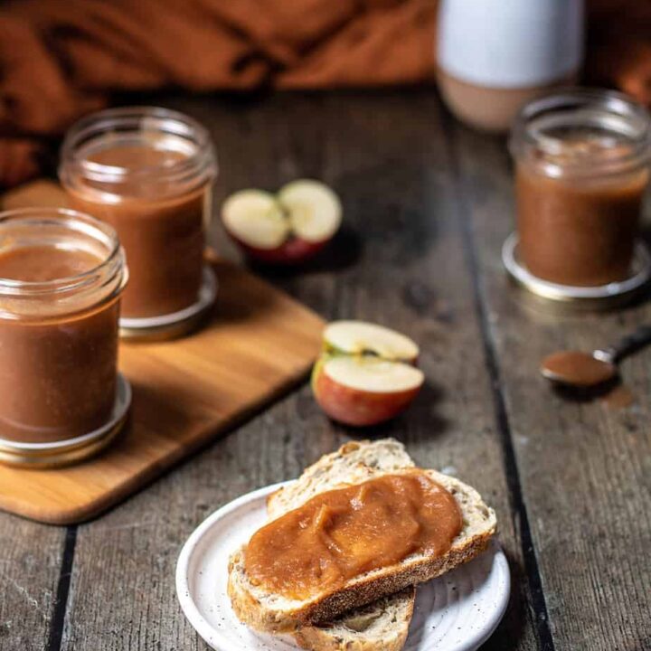 slices of bread with apple butter in the foreground, jars of apple butter in the background